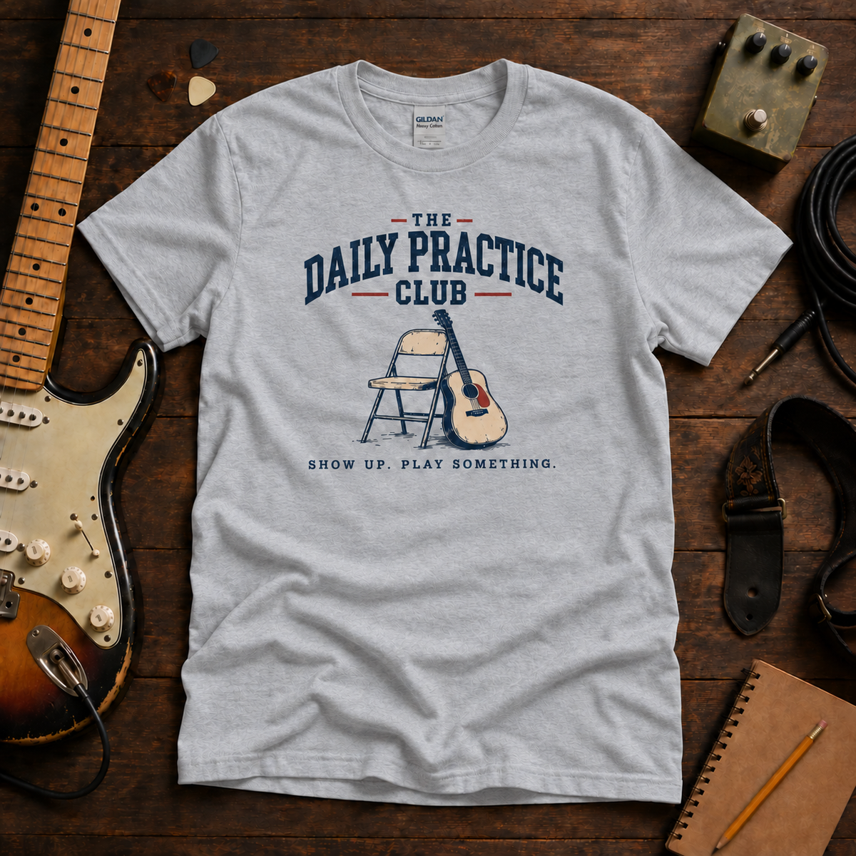 Daily Practice Club tee by Steady Strum, laid flat on a wood desk with guitar gear