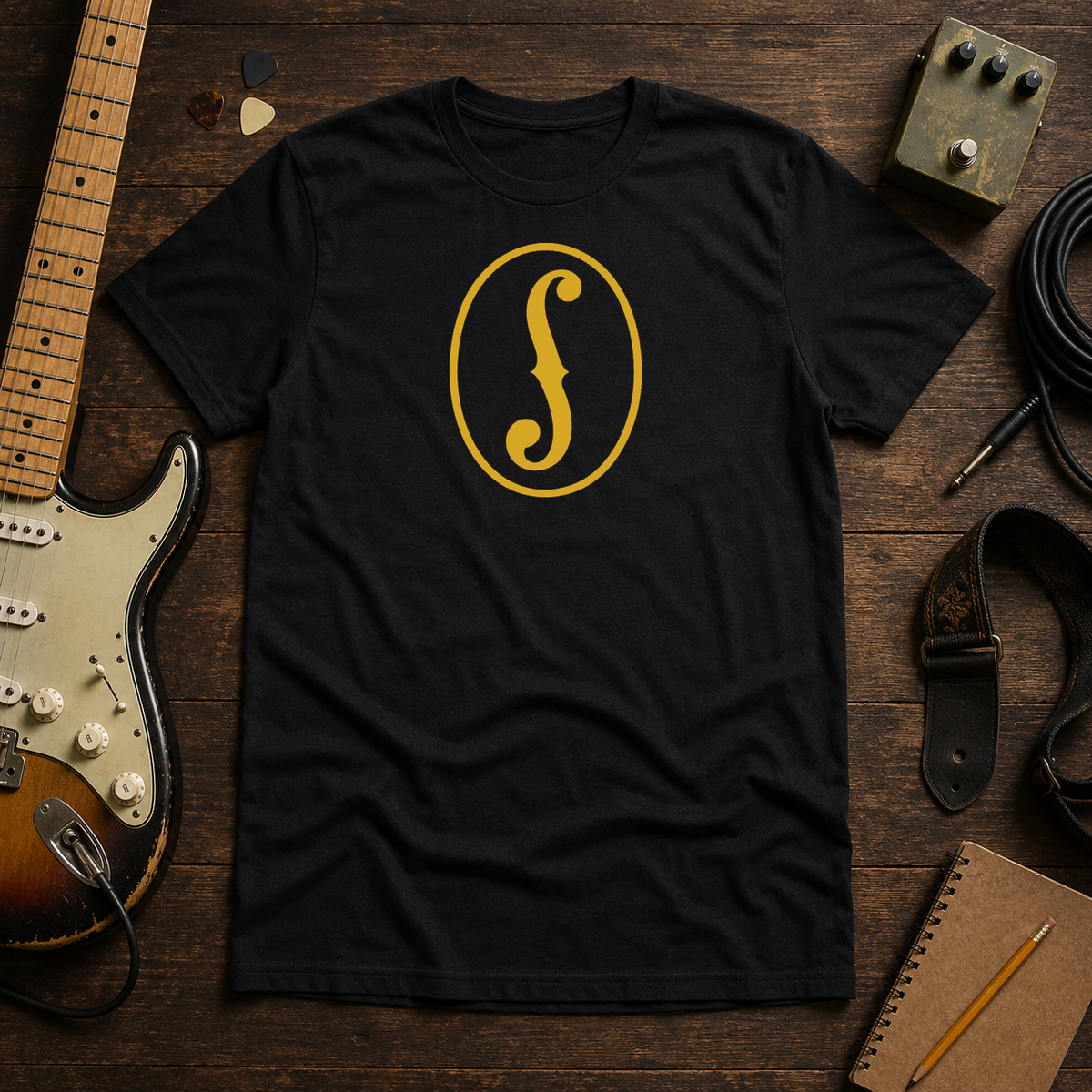 Black F-Hole tee by Steady Strum, laid flat on a wood desk with guitar gear