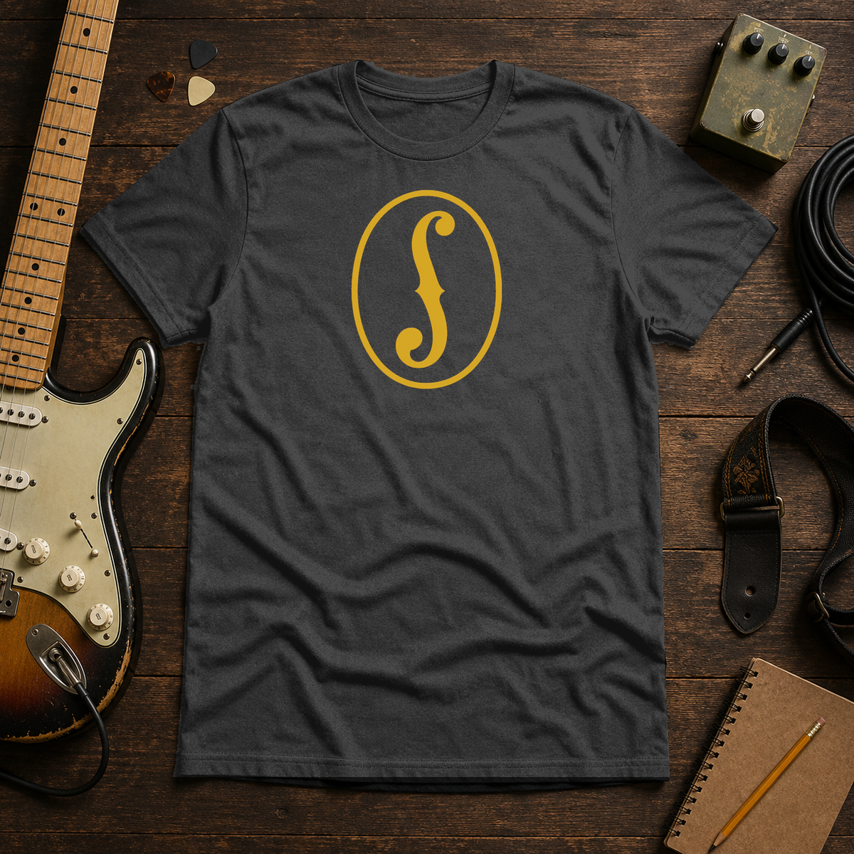 Dark Gray Heather F-Hole tee by Steady Strum, laid flat on a wood desk with guitar gear