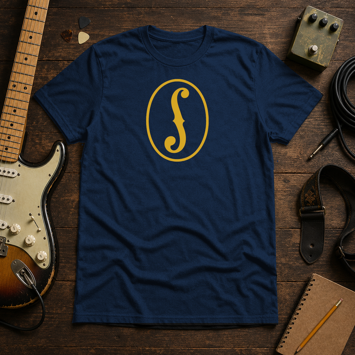 Navy F-Hole tee by Steady Strum, laid flat on a wood desk with guitar gear