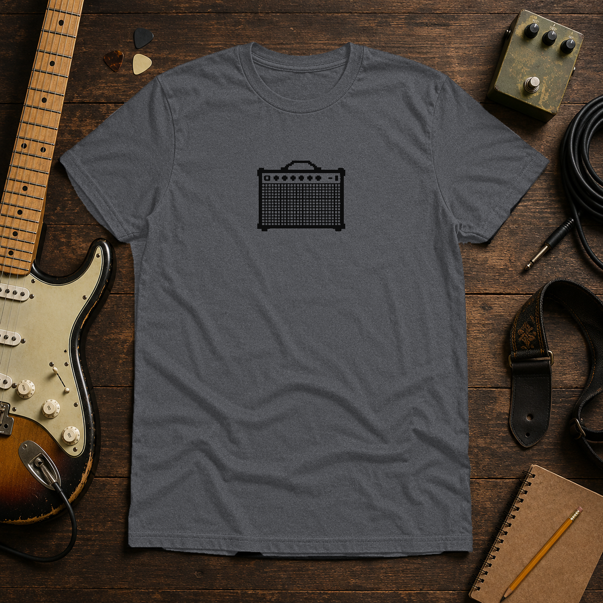 Graphite Heather Pixel Amp tee by Steady Strum, laid flat on a wood desk with guitar gear