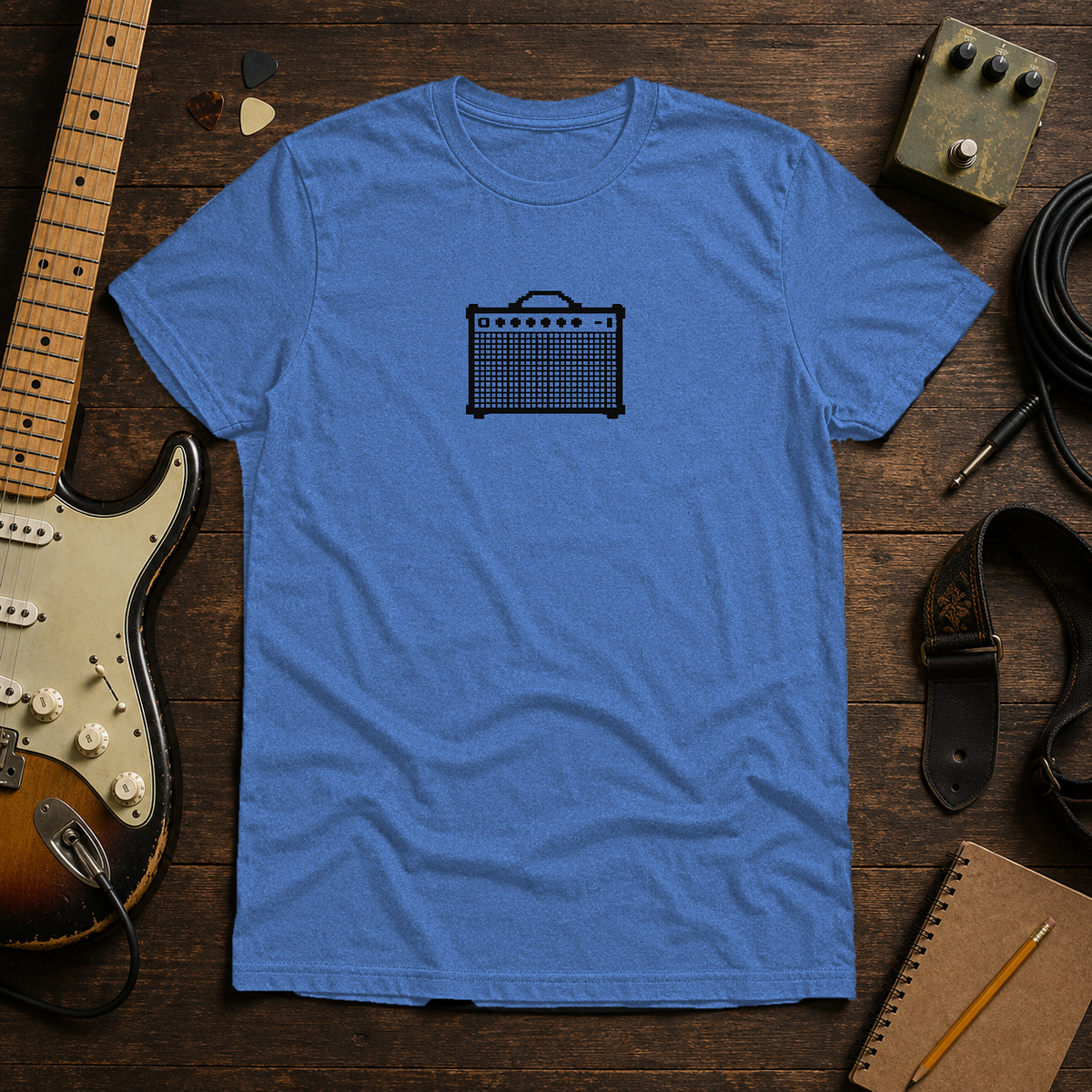 Heather Royal Pixel Amp tee by Steady Strum, laid flat on a wood desk with guitar gear