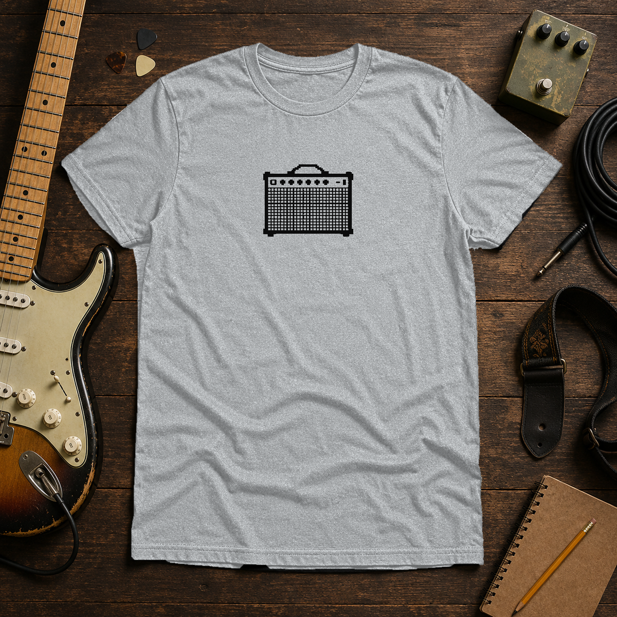 Sport Grey Pixel Amp tee by Steady Strum, laid flat on a wood desk with guitar gear
