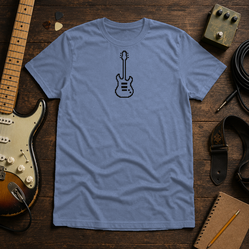 Heather Indigo Pixel Guitar tee by Steady Strum, laid flat on a wood desk with guitar gear