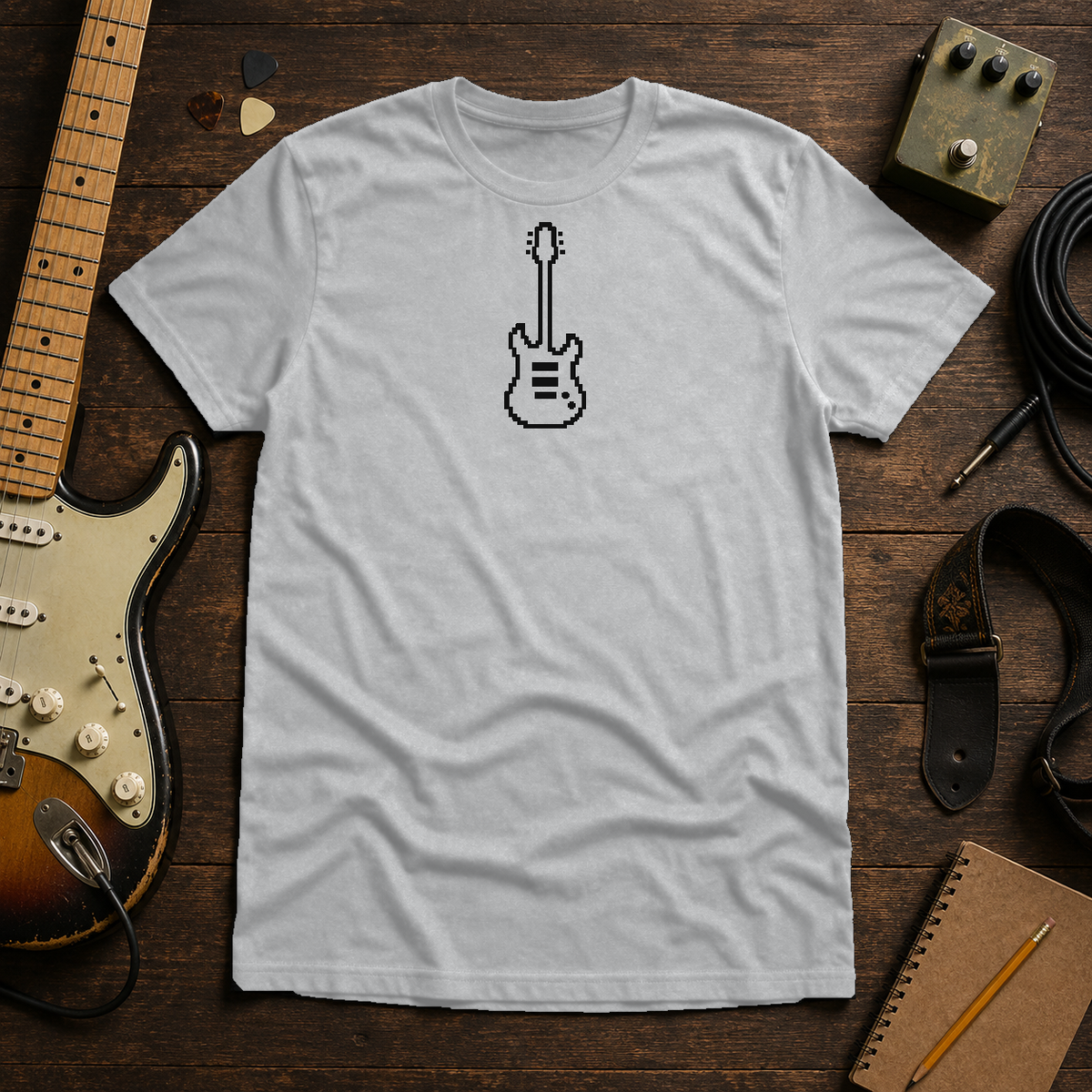 Sport Gray Pixel Guitar tee by Steady Strum, laid flat on a wood desk with guitar gear