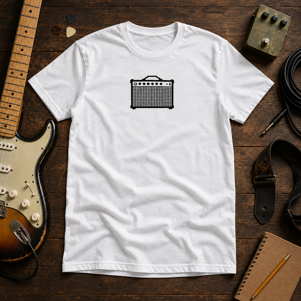 White Pixel Amp tee by Steady Strum, laid flat on a wood desk with guitar gear