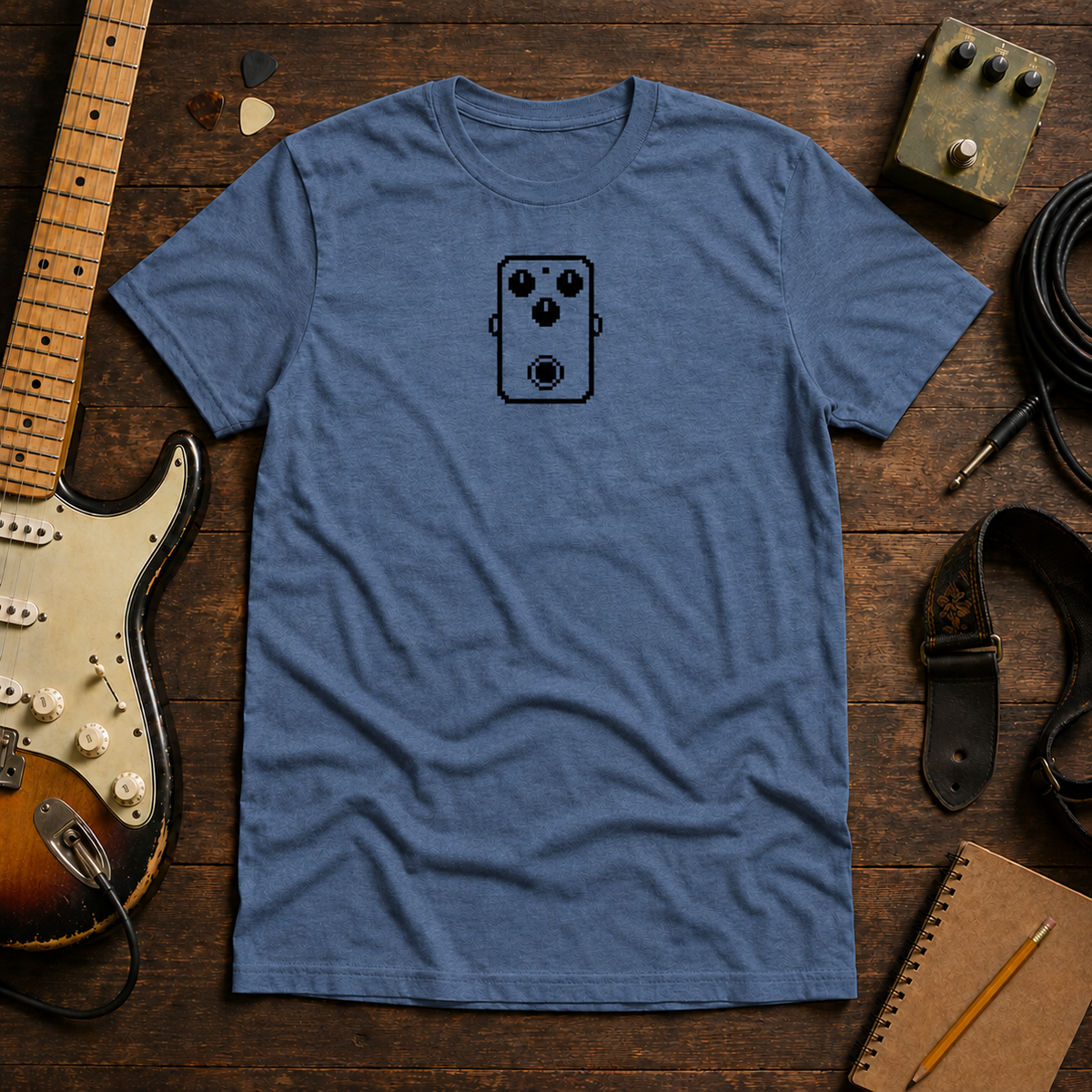 Indigo Pixel Pedal tee by Steady Strum, laid flat on a wood desk with guitar gear