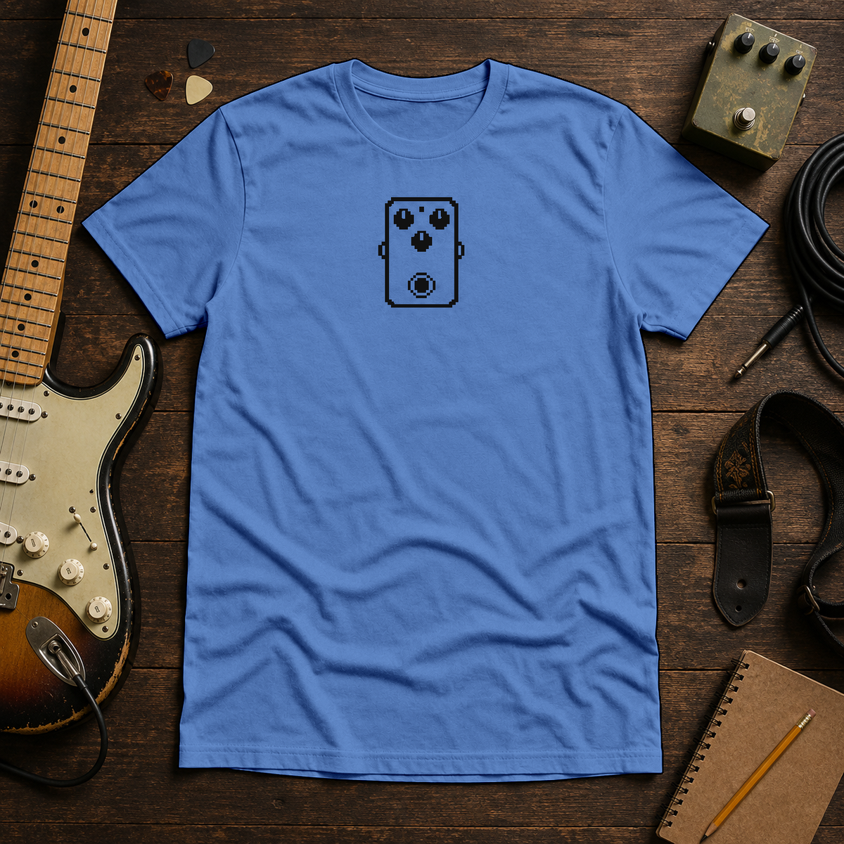Royal Pixel Pedal tee by Steady Strum, laid flat on a wood desk with guitar gear